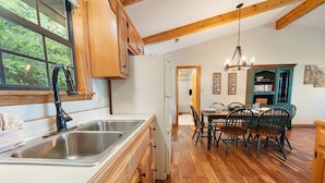 Una cocina con armarios de madera, un lavamanos de acero inoxidable y una zona de comedor con mesa y sillas.