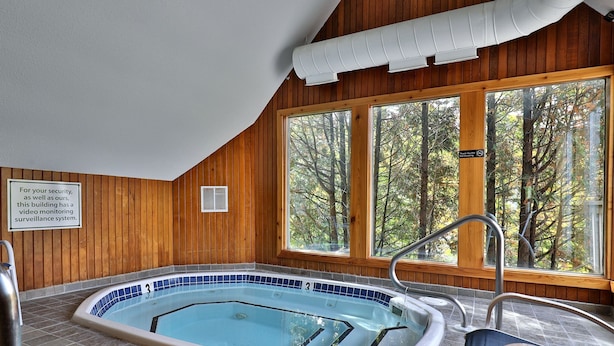 A wooden-paneled room with a hot tub, large windows, and a sign about a video monitoring surveillance system. - Fall Line Condo A5 1 Bedroom Condo (Killington)