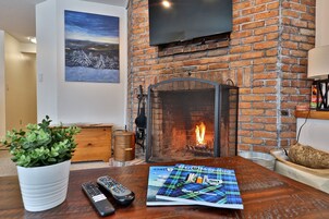 A living room with a brick fireplace, a mounted TV, a potted plant, and a magazine on the table.