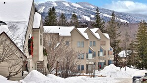 A multi-story building with a snow-covered roof and a view of a mountain range in the background. - Fall Line Condo A5 1 Bedroom Condo (Killington)
