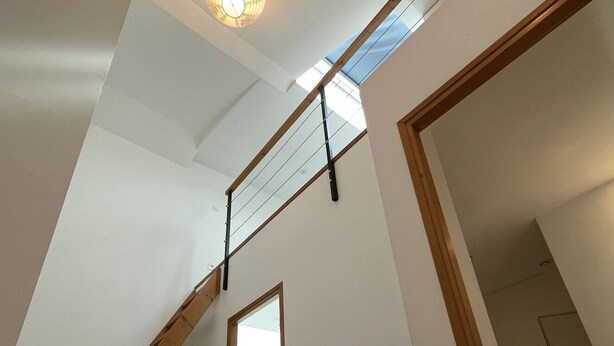 Un interior moderno con una escalera de madera, un tragaluz y vistas a otra habitación.