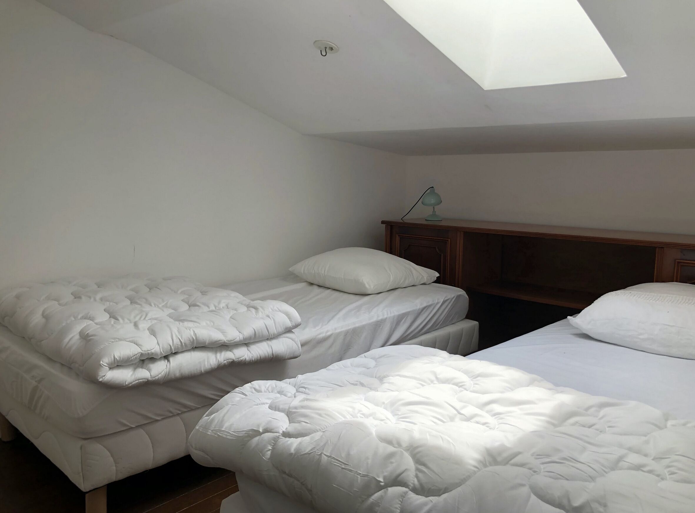 Une chambre avec deux lits, une tête de lit en bois et un puits de lumière.