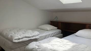 Une chambre avec deux lits, une tête de lit en bois et un puits de lumière.