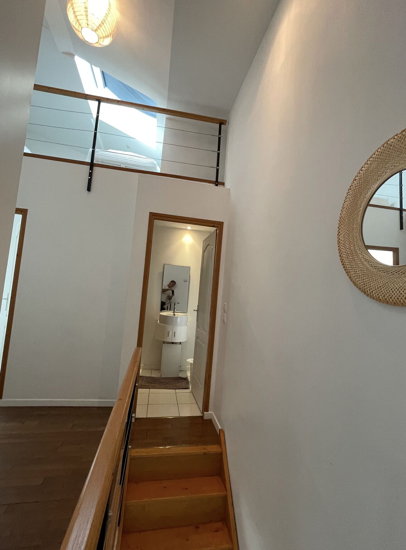 Una escalera conduce a un segundo piso con un tragaluz, un espejo redondo y un baño con lavamanos e inodoro a la vista.