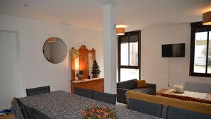 Un comedor con una mesa preparada para cuatro personas, un espejo, un árbol de Navidad y un televisor en la pared.