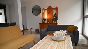 Una sala de estar con un sofá, una mesa de centro, un aparador de madera, un árbol de Navidad y un espejo en la pared.