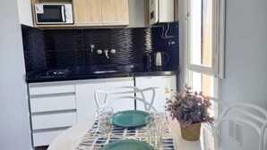 A compact kitchen with a black countertop, white cabinets, and a dining area with a table set for two. - Apartamento Céntrico y Luminoso (San Nicolas)