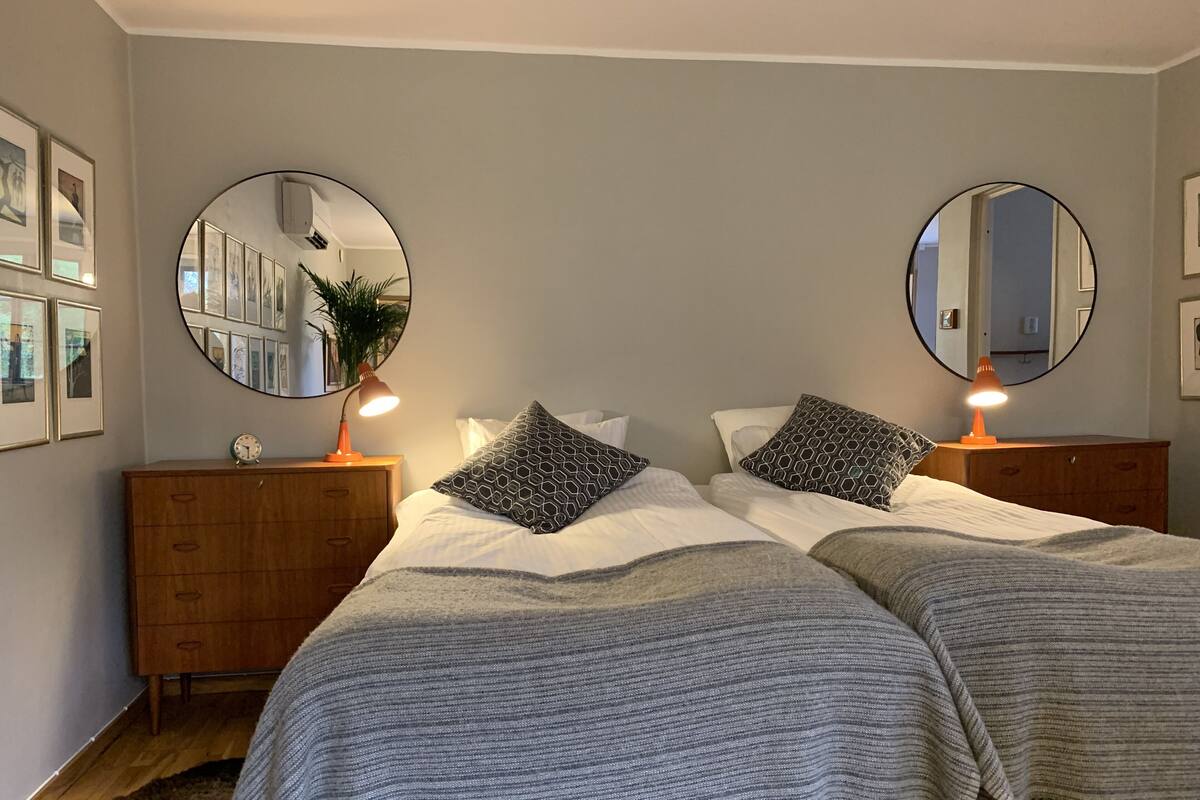 A bedroom with two beds, a wooden dresser, and two round mirrors on the walls.