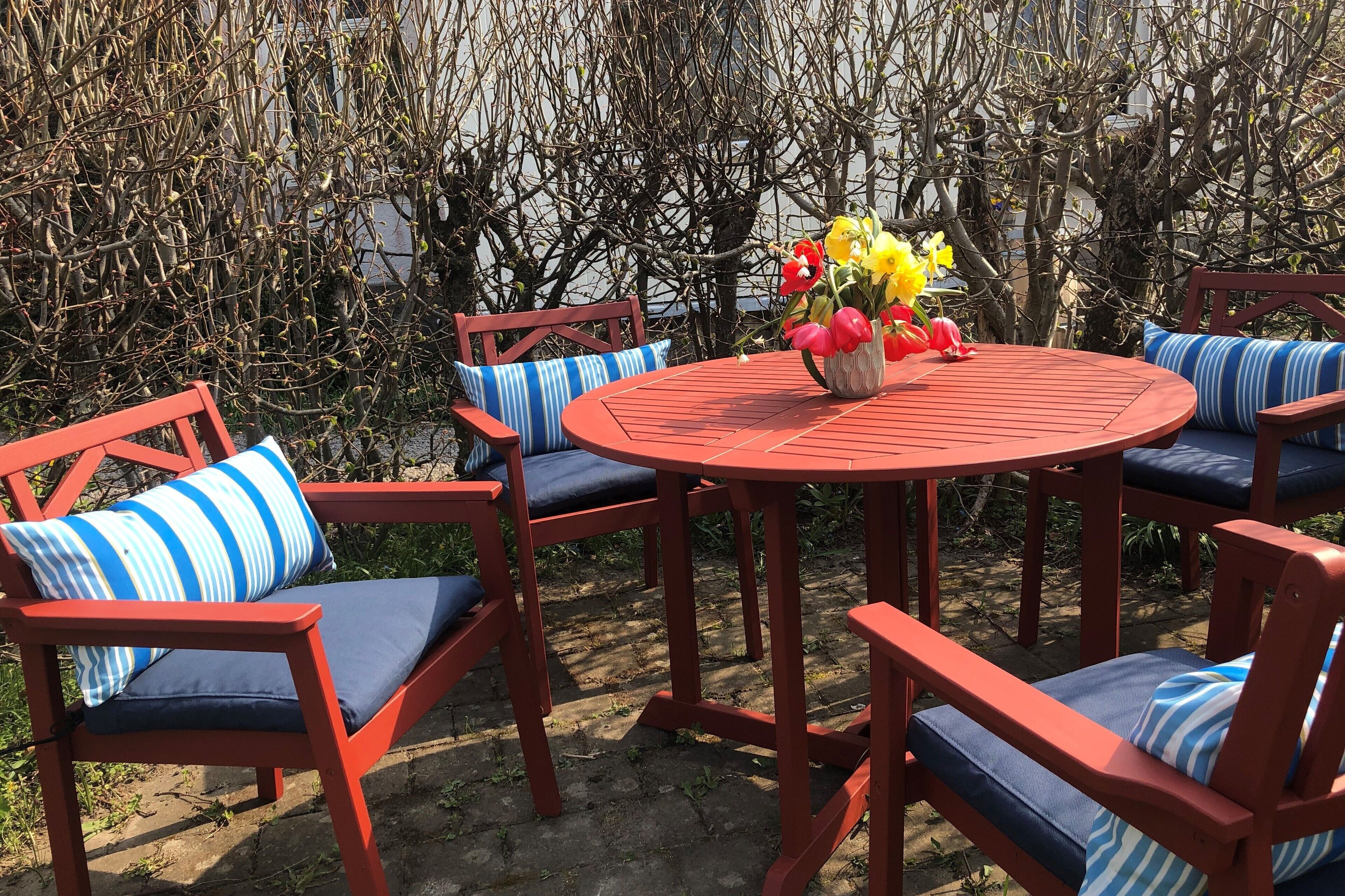 Ett runt, rött bord med blå, vadderade stolar och en vas med blommor.