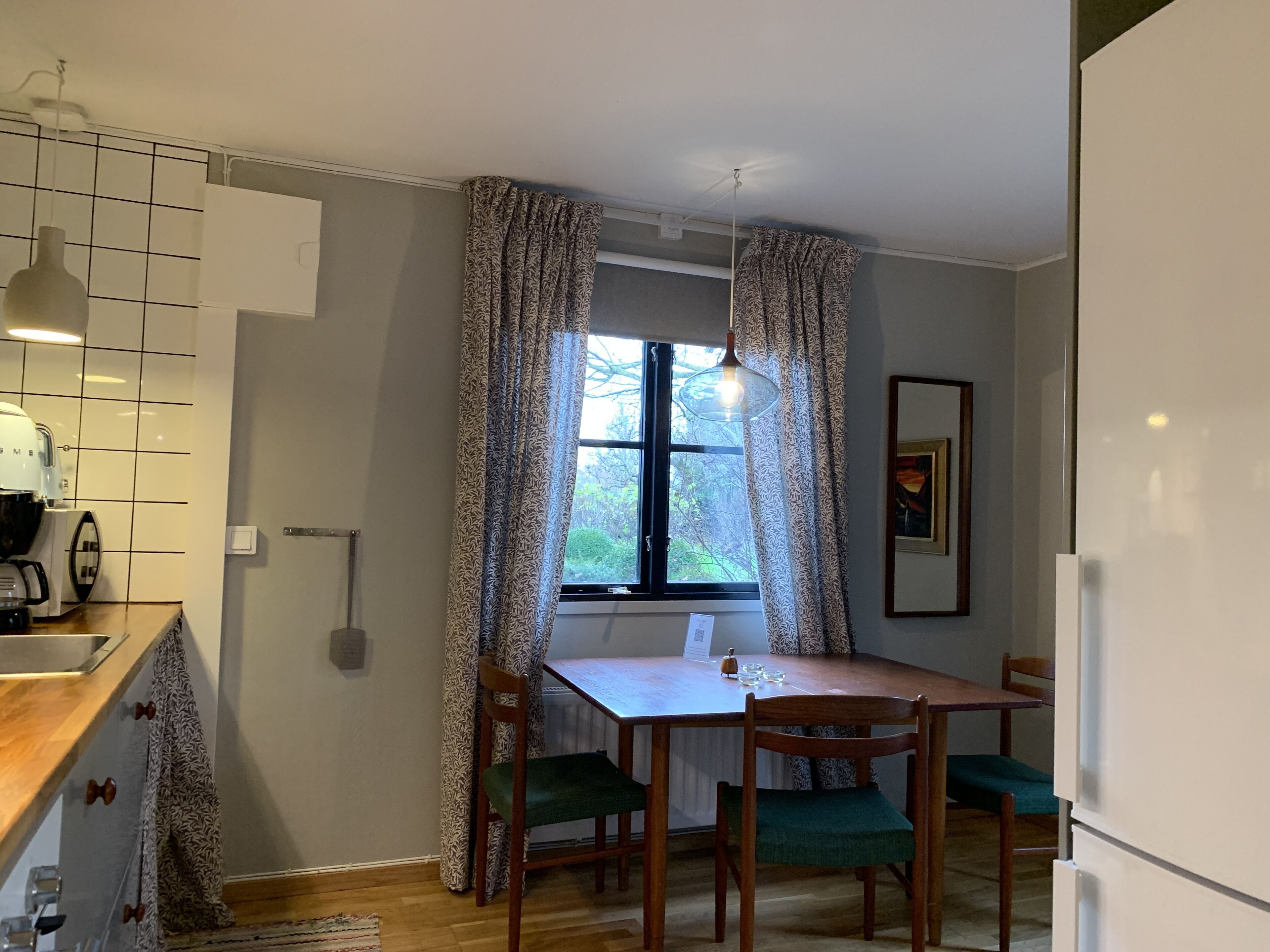 Una cocina compacta con una mesa de comedor, sillas, cafetera y una ventana con cortinas.