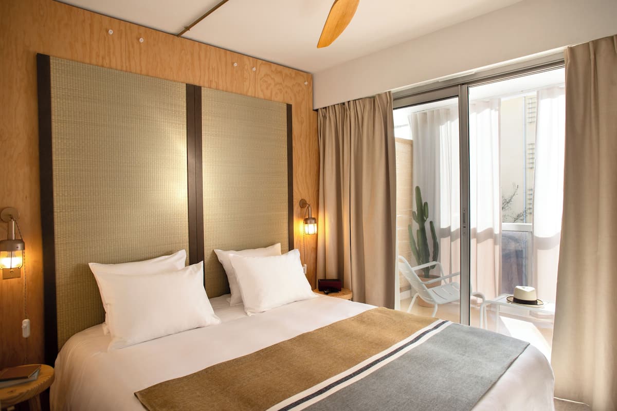 A hotel room with a large bed, a wooden headboard, a bedside table with a lamp, and a view of the balcony.