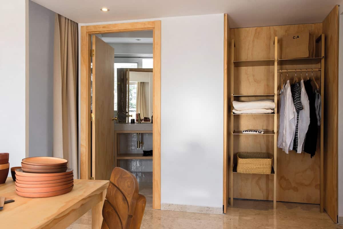 A wooden wardrobe with hanging space and shelves, a wooden table with plates, and a chair.