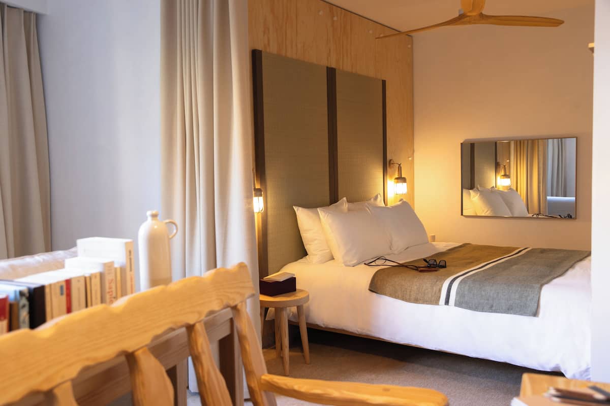 A hotel room with a bed, bedside table, and a mirror on the wall.