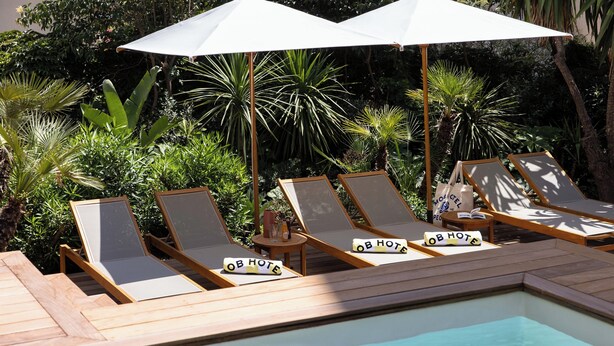 A poolside area with lounge chairs and umbrellas, surrounded by lush greenery. - MOB Hotel Cannes (Cannes)