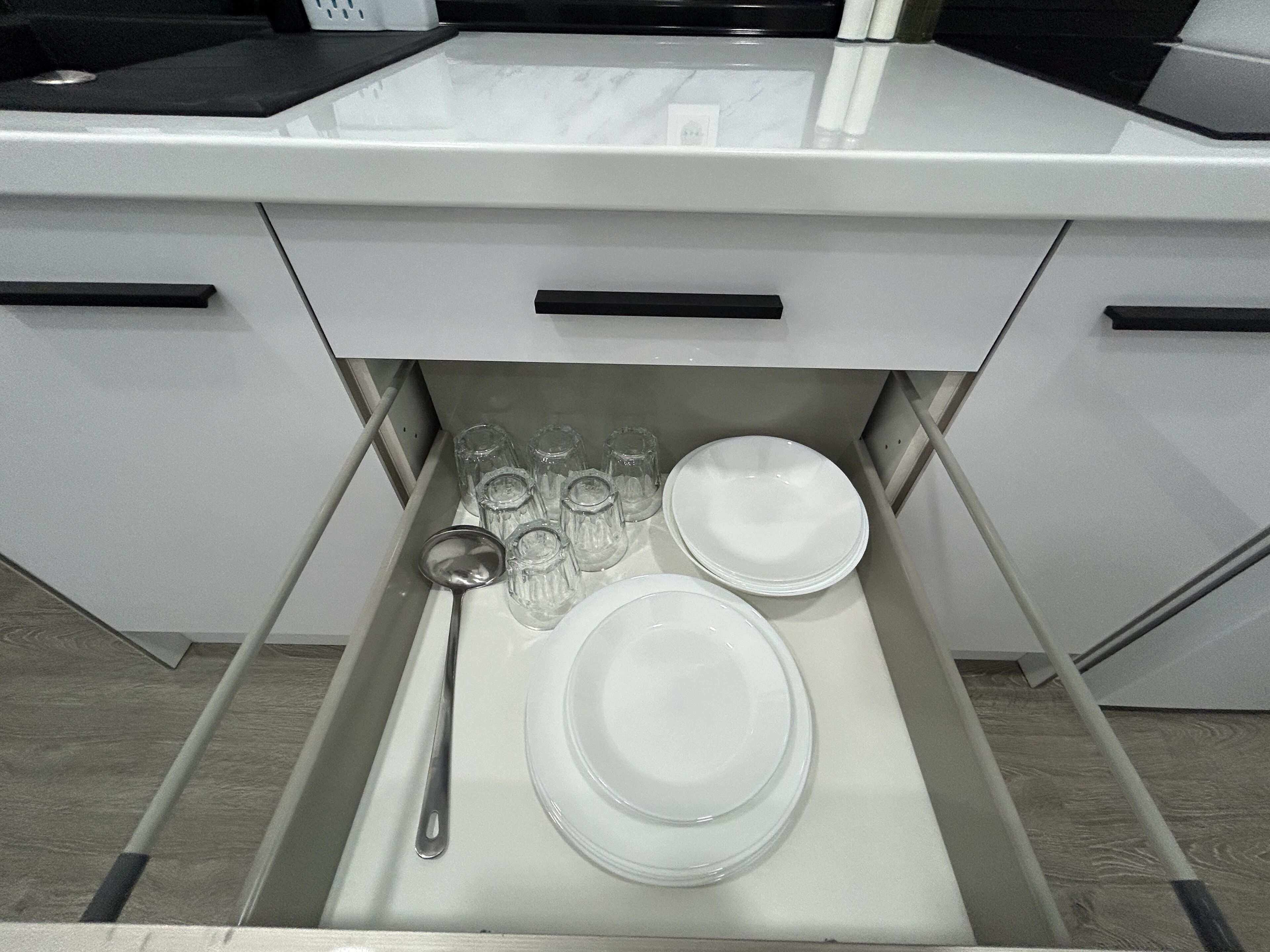 Un cajón de cocina con platos blancos, cristalería transparente y una cuchara de metal.