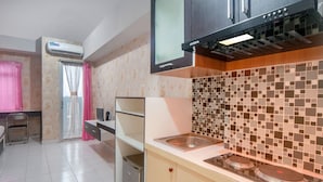 Een keuken met een magnetron, fornuis en spoelbak. Er is een raam met gordijnen en een deur naar een andere kamer.