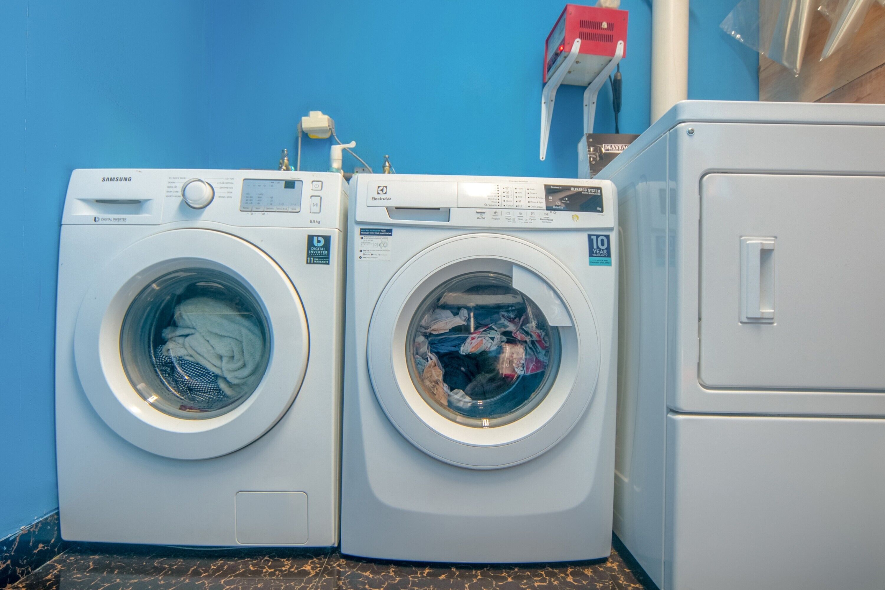 Two front-loading washing machines with digital displays, a red and white cabinet, and a blue wall.