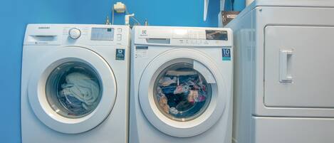 Two front-loading washing machines with digital displays, a red and white cabinet, and a blue wall.