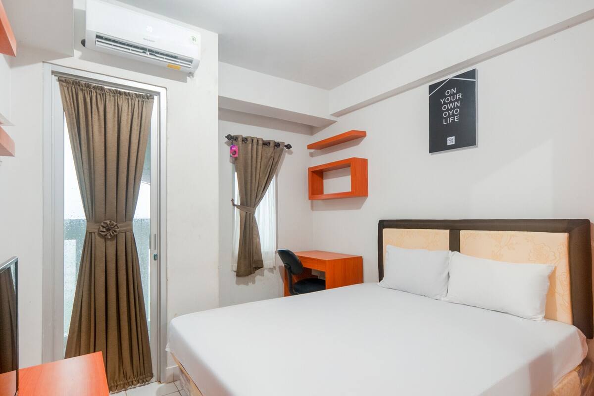 A hotel room with a bed, a desk, a chair, an air conditioner, and a window with curtains.