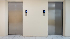 Twee liftdeuren met digitale schermen, een effen muur en een betegelde vloer.