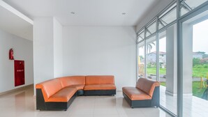 Een modern interieur met een ruime modulaire bank, een brandblusser en een glazen wand met uitzicht op de omgeving.