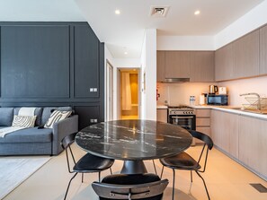 A modern kitchen with a dining area, featuring a round table, chairs, a sofa, and built-in cabinets. - The Elevated Abode 1BHK Apt in Downtown (Dubai)