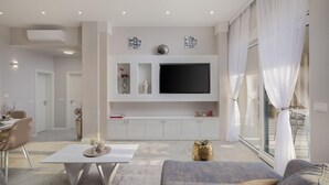 Ein modernes Wohnzimmer mit Flachbildfernseher, weißen Schränken und einem großen Fenster mit weißen Vorhängen.