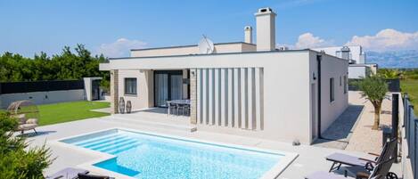 Ett modernt hus med en swimmingpool, en uteplats och utsikt över bergen.
