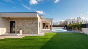 Ein modernes Haus mit Naturstein-Fassade, einem Schwimmbad und einem gepflegten Rasen.