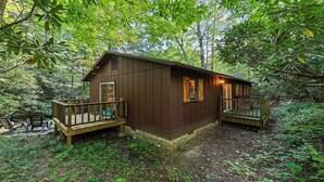 A wooden cabin with a deck, surrounded by dense forest. - Huckleberry Hideaway (Maggie Valley)