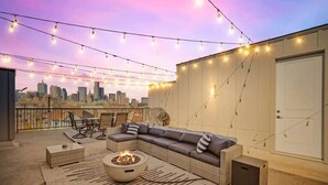 An outdoor living area with a sofa, fire pit, and string lights. - 3-BD Luxury Living w Rooftop Garden Views (Dallas)