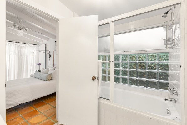 A modern bathroom with a bathtub, a shower, and a window with a view of greenery. - SUN DAY, FUN DAY ~ Renovated 2/2 Home 2 Blocks from Beach in Casa Marina! (Key West)