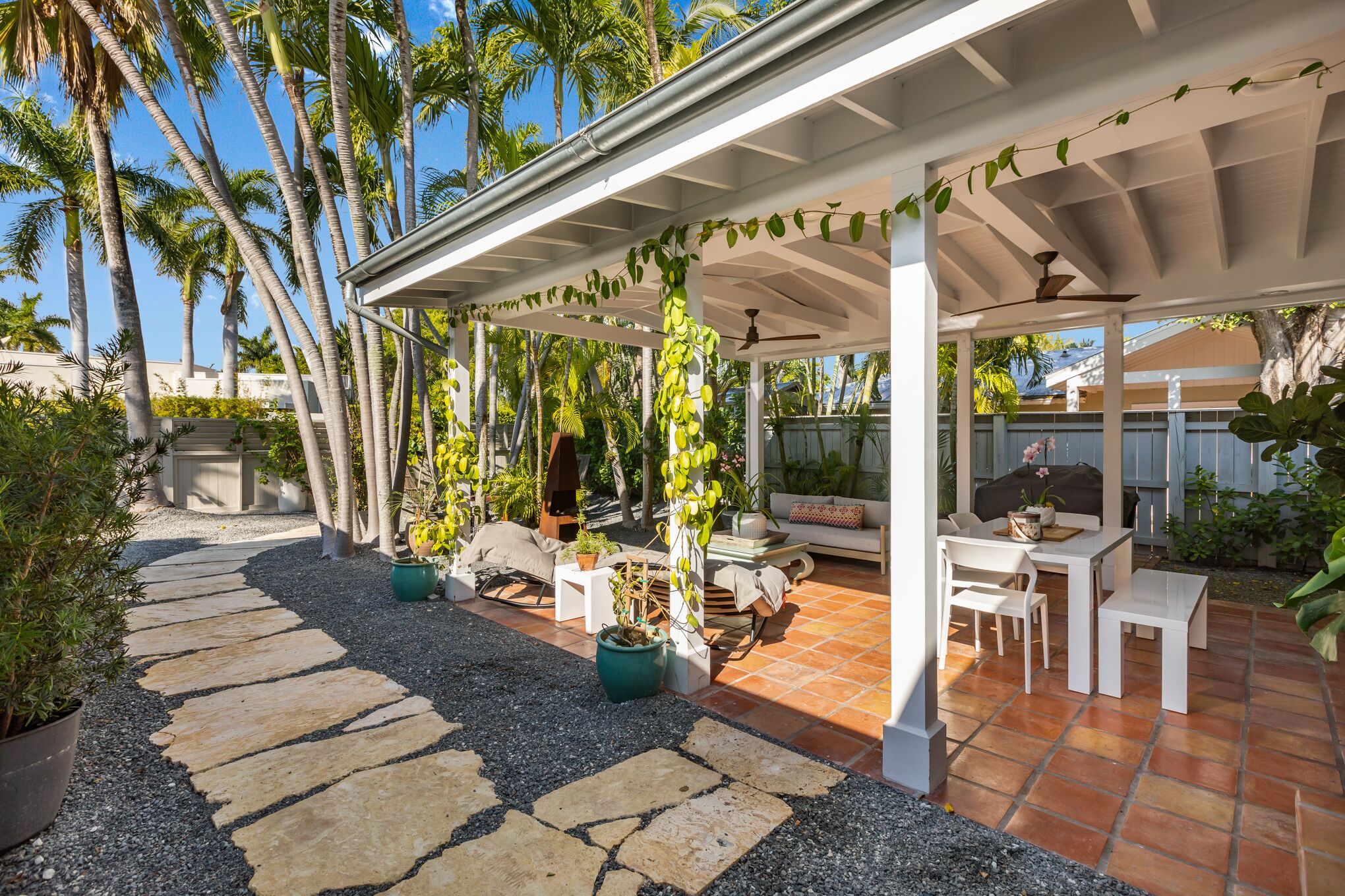 A covered patio area with a stone pathway, outdoor furniture, and potted plants.
