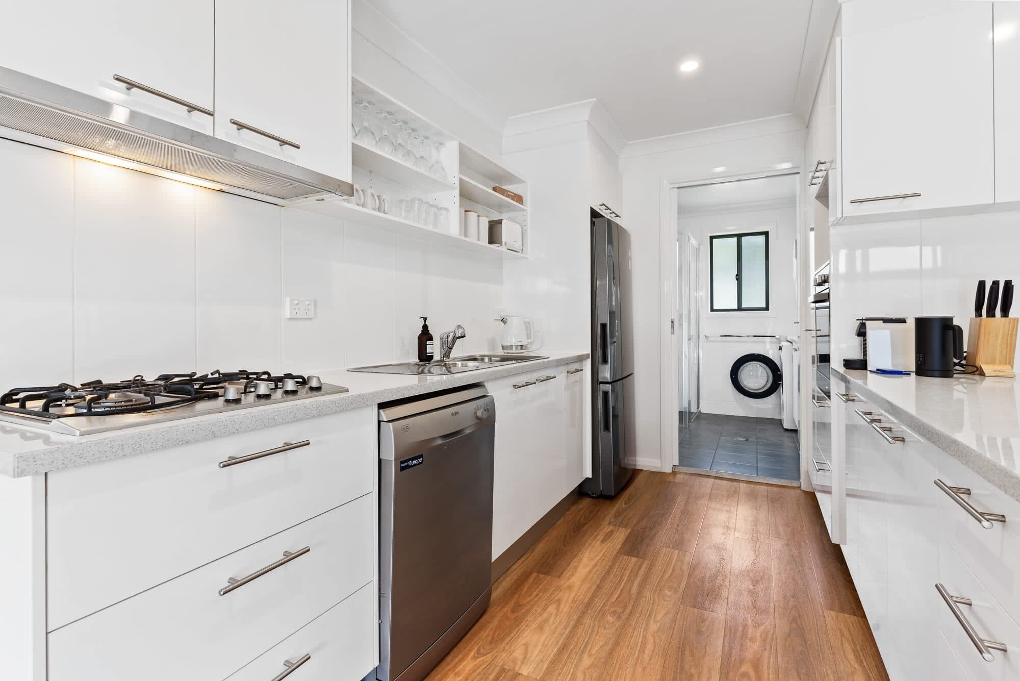 Una cucina moderna con mobili bianchi, elettrodomestici in acciaio inossidabile e pavimento in legno.