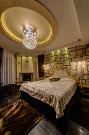 A luxurious bedroom with a large bed, a fireplace, a stone wall, and a chandelier.