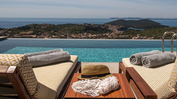 Zona de piscina con dos sillones reclinables, toallas, un sombrero y una mesa.