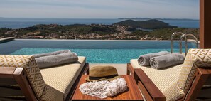 Zona de piscina amb dues gandules, tovellons, un barret i una taula.