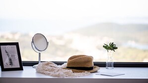 Una ventana con un certificado enmarcado, un espejo redondo, un sombrero de paja, un adorno de crochet y una pequeña planta en maceta.