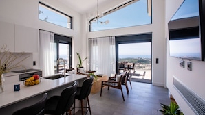 A modern kitchen with a central island, dining area with chairs, large windows, and a view of the landscape.