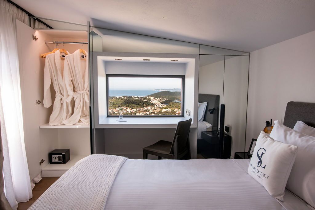 Une chambre d’hôtel comprenant un lit, une chaise, un bureau, un miroir, une fenêtre donnant sur la ville et un porte-peignoir.