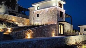 A modern building with a stone facade, multiple levels, and outdoor lighting. - GV Sivota Luxury Villa - SL2022 (Igoumenitsa)