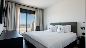 A modern hotel room with a large bed, a desk, and a view of the outdoors. - GV Sivota Luxury Villa - SL2021 (Igoumenitsa)