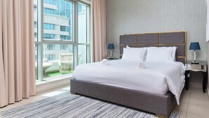 A modern hotel room with a large bed, two bedside lamps, a view of a building through a window, and a balcony with outdoor furniture. - BellaVista - Spectacular - 2 BR Penthouse - Boulevard Central - Panoramic Terrace & Burj Khalifa Vie (Dubai)