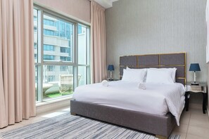 A hotel room with a large window, a bed with white linens, a grey headboard, two bedside tables with lamps, and a view of a building outside. - BellaVista - Spectacular - 2 BR Penthouse - Boulevard Central - Panoramic Terrace & Burj Khalifa Vie (Dubai)
