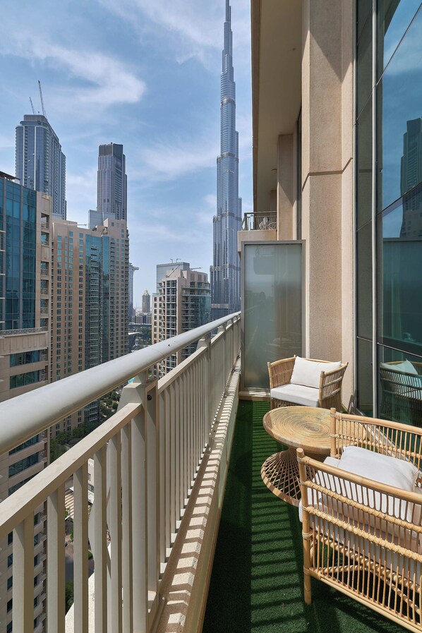 A balcony with wicker furniture, a view of tall buildings, and a glass railing.