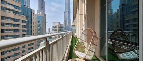 A balcony with a hanging chair, a small table, and a view of tall buildings.