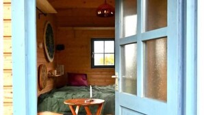 A wooden cabin room with a bed, a small table, and a window.