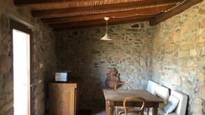 A stone-walled room with a wooden table and chairs, a bench, and a hanging light fixture. - Delightful  house typical of the Sardinian countryside in the Monte Arcosu Park. (Località Macchiareddu-Grogastu I)