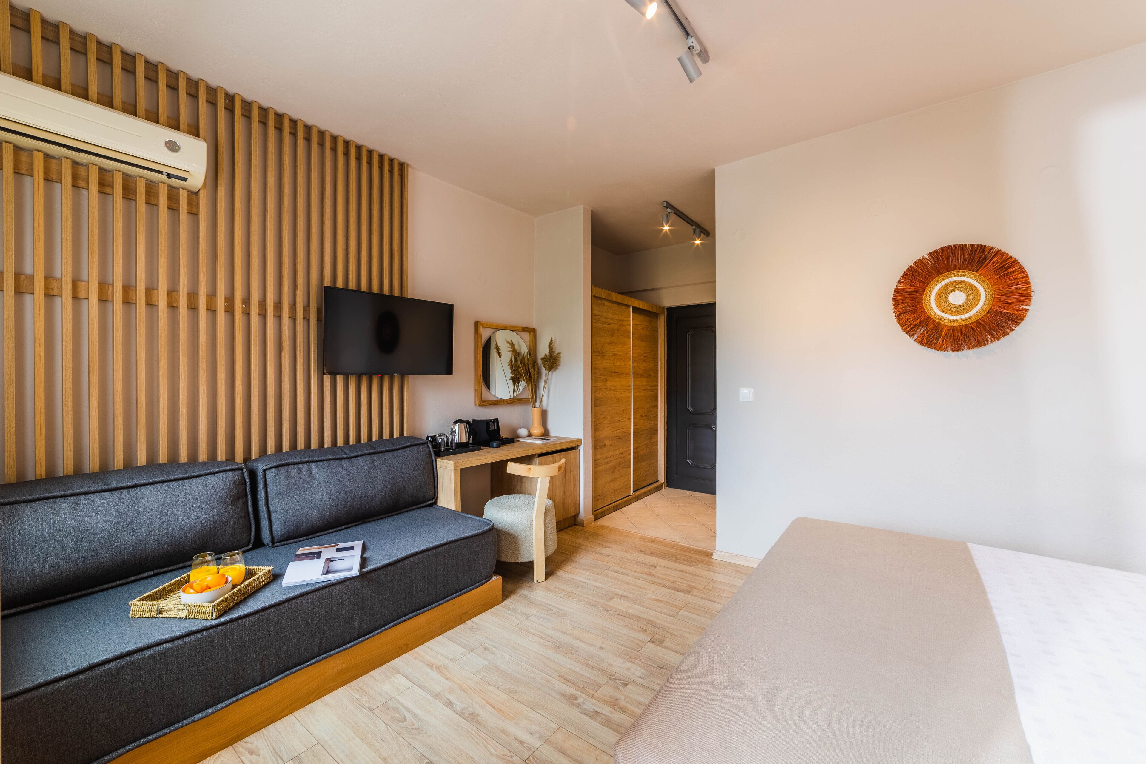 A modern hotel room with a sofa, a small desk, a flat-screen TV, and a decorative wall piece.