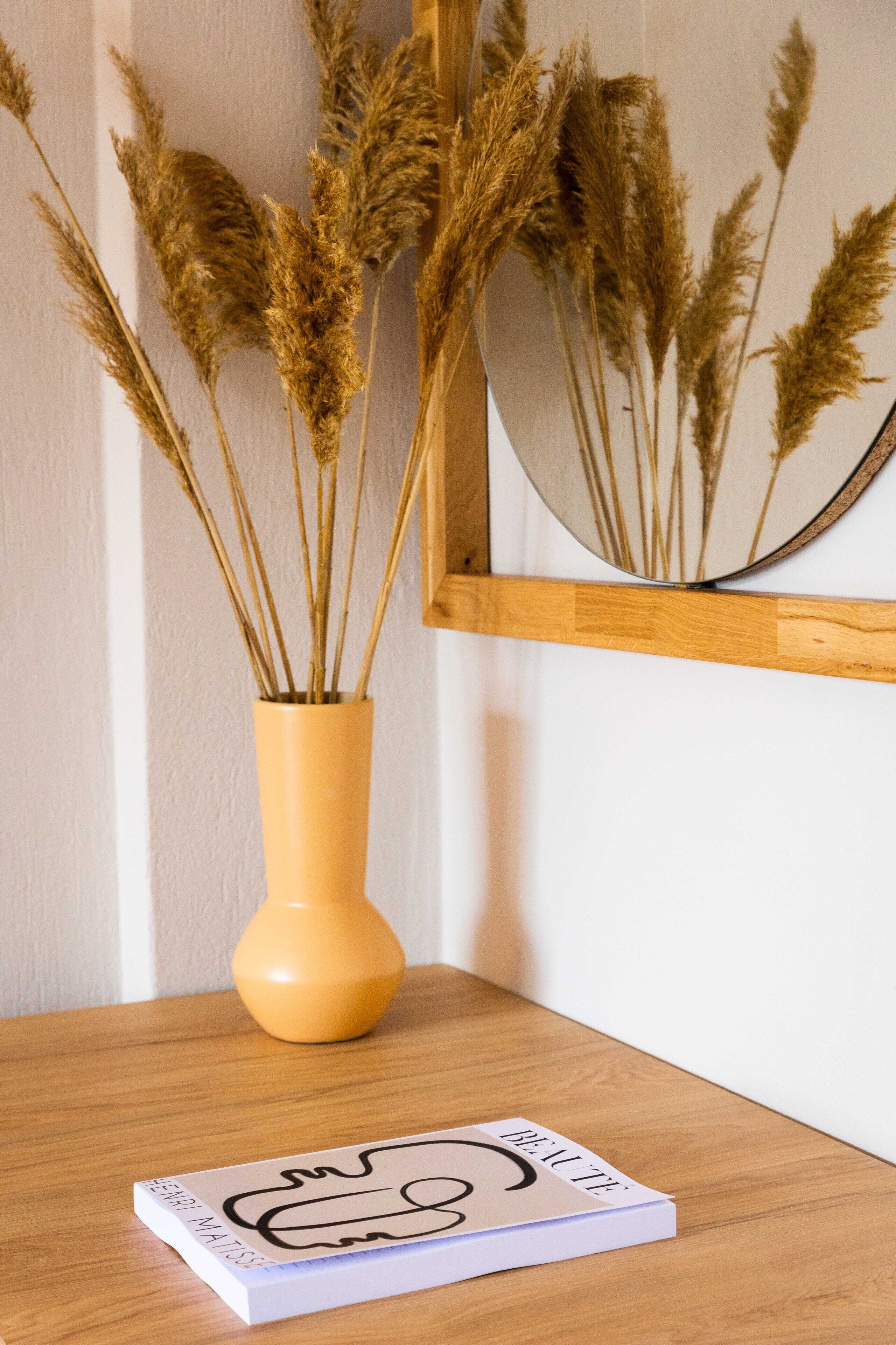A wooden table with a vase of dried pampas grass and a book titled "BEAUTY".